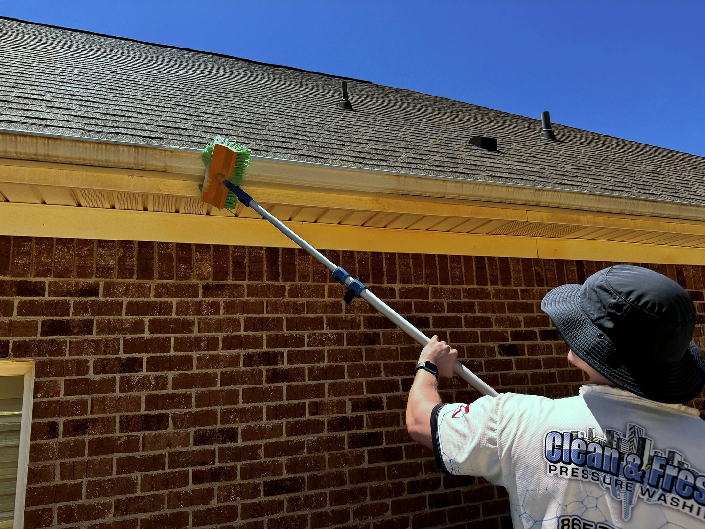Clean and Fresh technician brushing the outside face of a gutter on a brick home