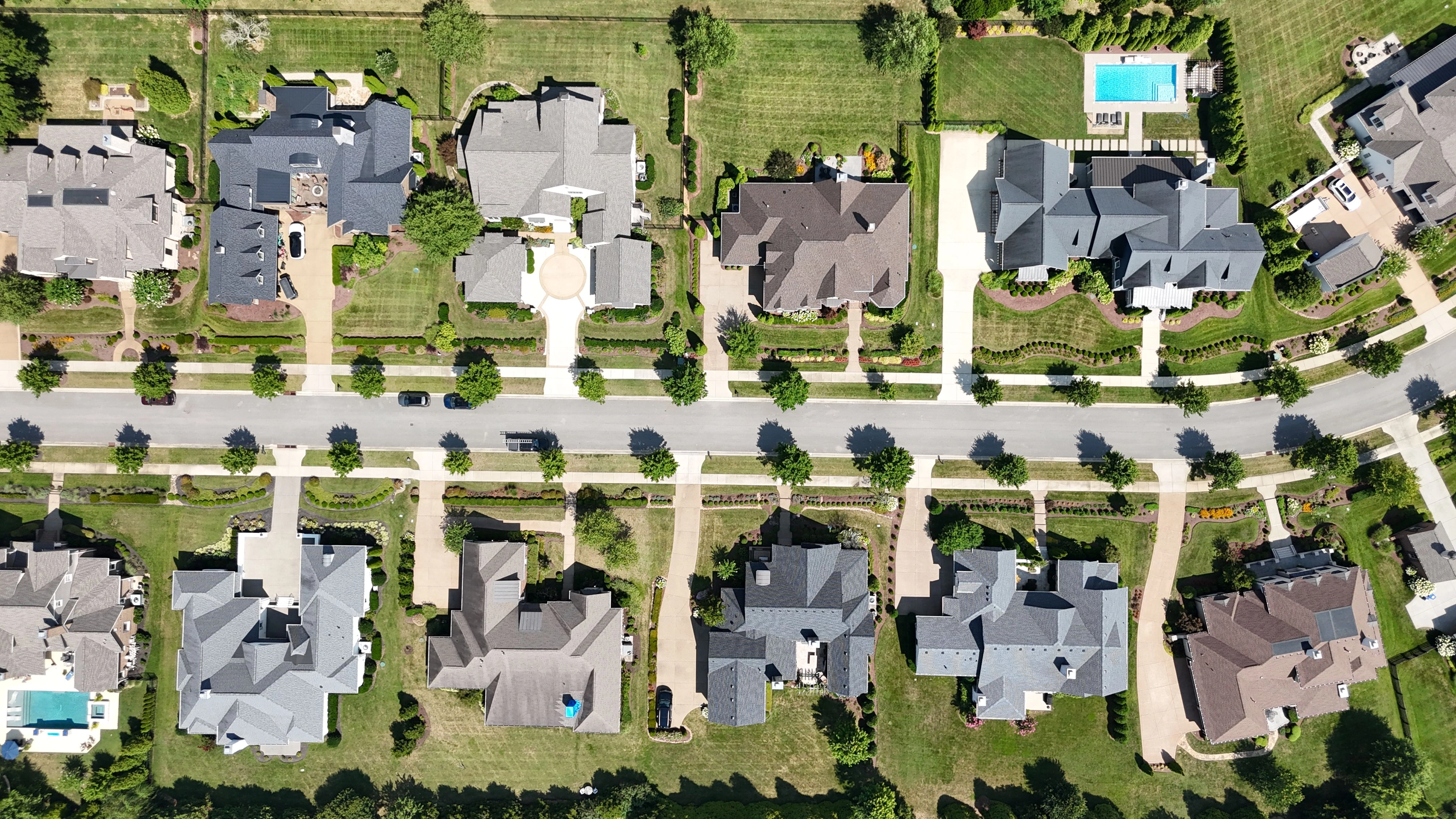 Overhead view of a tree-lined residential street with sidewalks, curbs and driveways between two rows of homes