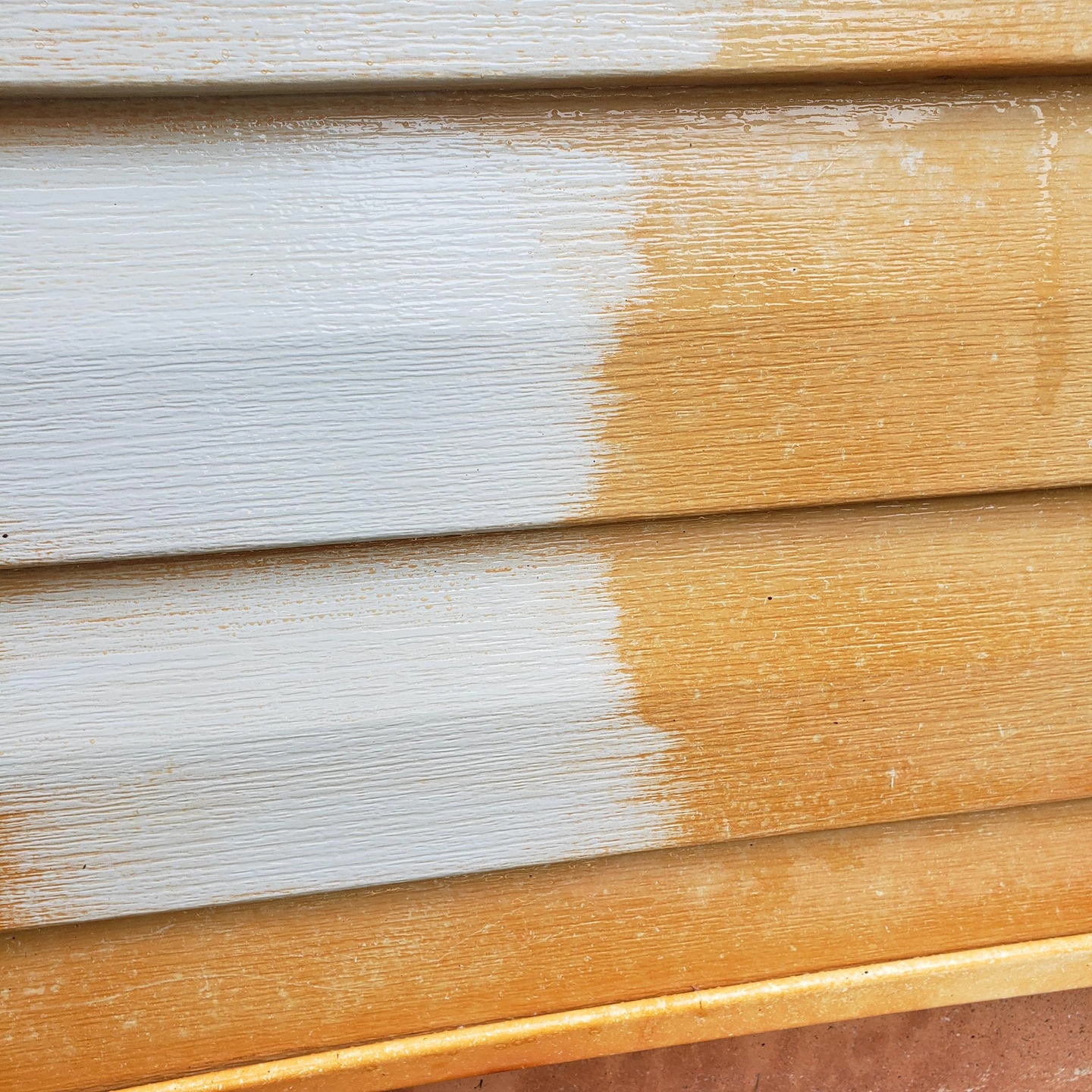 Red clay staining beside a cleaned section of white siding, with the original surface texture visible