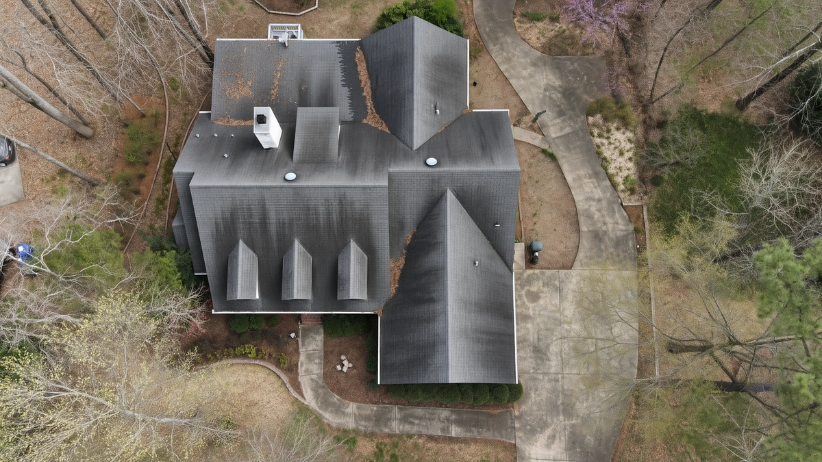 Illustrative aerial view of a house with strong black roof streaks and a dirty curved concrete driveway