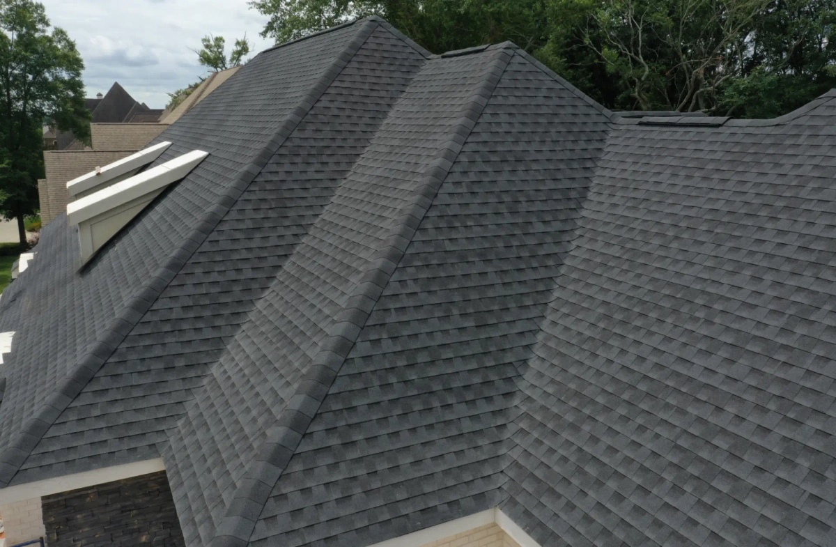 A gray asphalt-shingle roof with darker and lighter tones across intersecting roof slopes